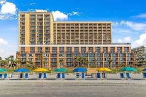 Een hotel met meerdere verdiepingen, een ruim balkon en zitplaatsen aan het strand.