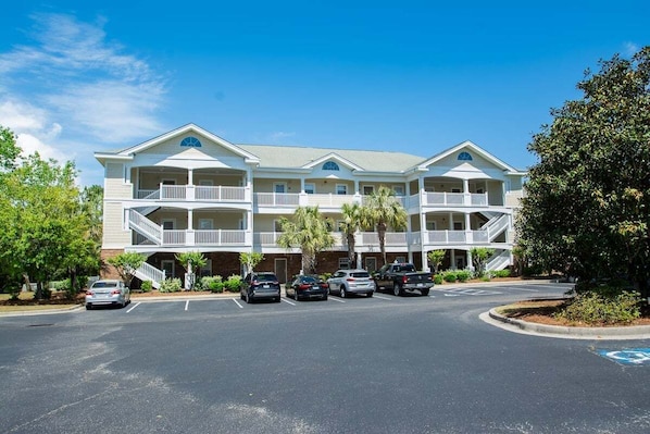 A multi-story hotel with a central atrium, balconies, and a parking lot with several cars.