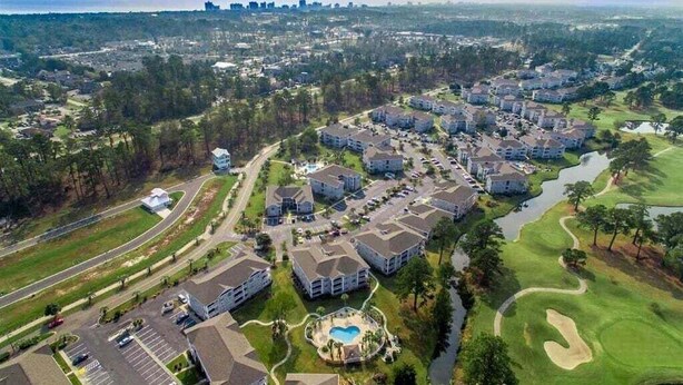 Vue aérienne d’un quartier résidentiel comprenant plusieurs immeubles d’appartements, un terrain de golf et une piscine.