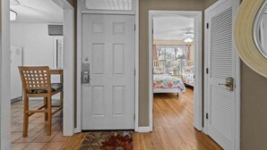 Un pasillo con una puerta blanca, una silla de madera y una cama en la habitación contigua.