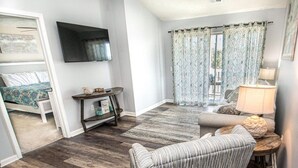 A living room with a striped armchair, a television mounted on the wall, a small table with a lamp, and a patterned curtain. - Nicely Decorated 2Br condo w/Great Waterway Views! (Myrtle Beach)