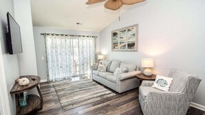 A living room with a grey sofa, a striped armchair, a wooden coffee table, and a TV mounted on the wall. - Nicely Decorated 2Br condo w/Great Waterway Views! (Myrtle Beach)