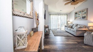A living room with a wooden coffee table, a sofa, a ceiling fan, and a large mirror. - Nicely Decorated 2Br condo w/Great Waterway Views! (Myrtle Beach)