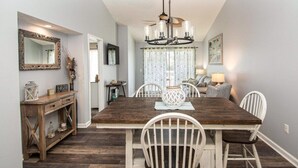 A dining area with a wooden table, white chairs, a chandelier, and a mirror on the wall. - Nicely Decorated 2Br condo w/Great Waterway Views! (Myrtle Beach)