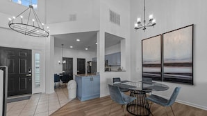 Eine geräumige Küche mit einer zentralen Kochinsel, einem Essbereich mit rundem Tisch und blauen Stühlen sowie einem großen Gemälde an der Wand.
