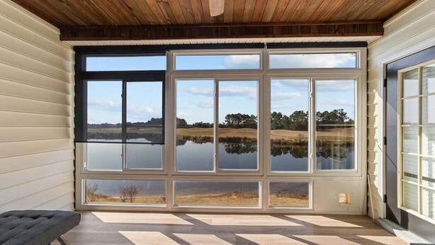 Ein Zimmer mit großen Fenstern und Blick auf einen See und Bäume.