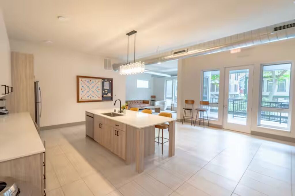 A spacious kitchen with a central island, a dining area with chairs, and large windows offering a view of the outside.