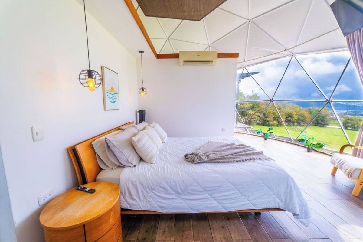A bedroom with a bed, bedside table, and a view of the outdoors.