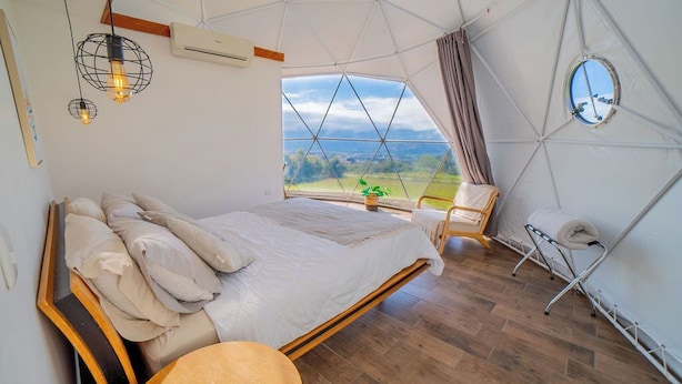 A bedroom with a large bed, a round table, a chair, and a view of the outdoors. - Tocuma Glamping (San Rafael)