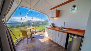 A kitchen with a large window, a dining table, and a refrigerator. - Tocuma Glamping (San Rafael)