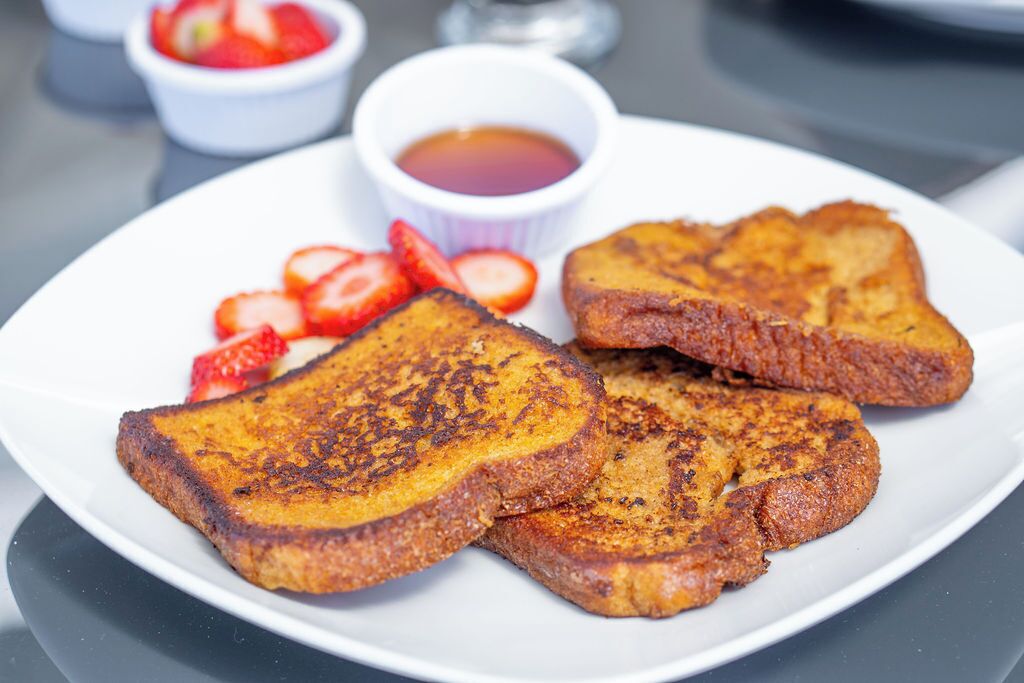 A plate of French toast with strawberries and syrup.