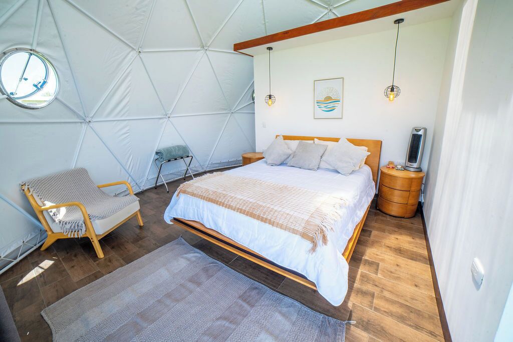 A bedroom with a bed, a chair, a bedside table, a heater, and a window.
