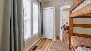 A room with a bunk bed, a door leading to another room, a window with blinds, and a patterned rug on the floor. - Oliver Twist Cottage - Walk to Downtown - Hot Tub & Grill-Cozy Charm (Chattanooga)