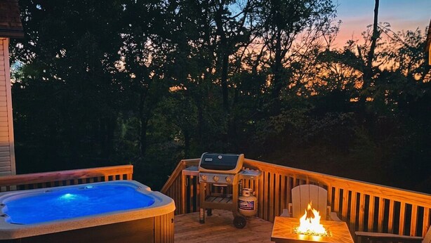 A wooden deck with a hot tub, grill, and fire pit, surrounded by trees. - Oliver Twist Cottage - Walk to Downtown - Hot Tub & Grill-Cozy Charm (Chattanooga)