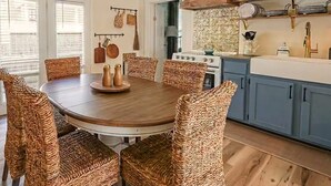 A dining room with a round table and wicker chairs, a kitchen with blue cabinets and a stove, and a chandelier. - Oliver Twist Cottage - Walk to Downtown - Hot Tub & Grill-Cozy Charm (Chattanooga)