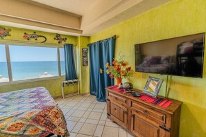 Una habitación con cama, televisión, mueble de madera, ventana con cortinas y vista al mar.