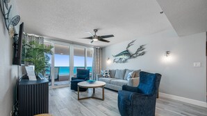 Ein modernes Wohnzimmer mit Sofa, Ohrensessel und Couchtisch, einem Deckenventilator und Meerblick durch große Schiebetüren.