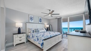 Ein Schlafzimmer mit einem Bett, Nachttischen, einem Deckenventilator und Blick auf den Ozean.