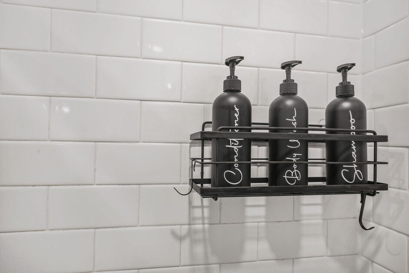 A black metal shelf with three black bottles against a white tiled wall.