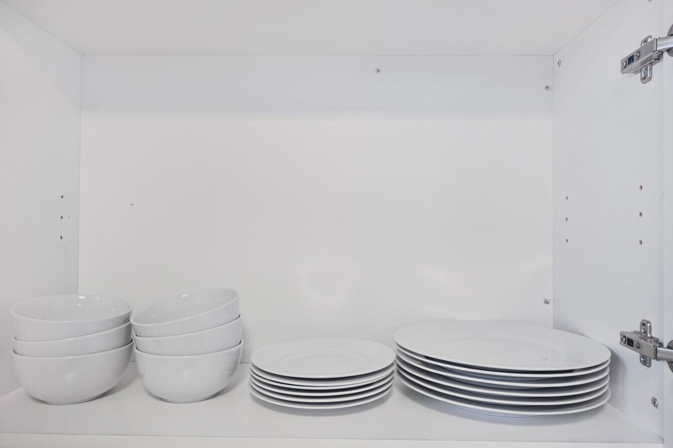 A white room with a stack of white bowls and plates on the floor.