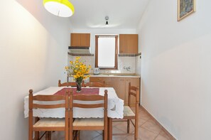 A dining area with a table set for four, a vase with yellow flowers, wooden chairs, and a window above the sink. - Apartment 2412/168845 (Istria - Premantura), 1000m from the beach (Premantura)