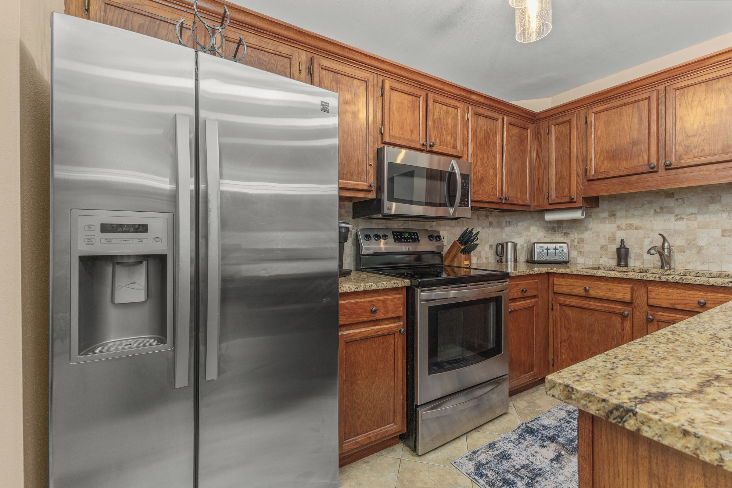 A kitchen with stainless steel appliances, wooden cabinets, granite countertops, and a built-in microwave.