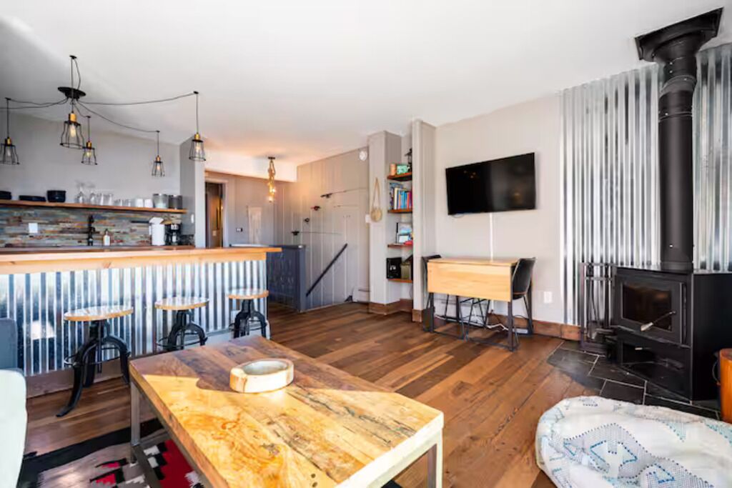 A modern kitchen with a bar area, a fireplace, and a dining space with a wooden table.
