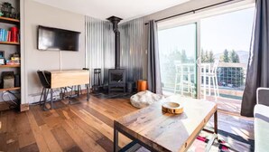 Un salon moderne doté d’une cheminée, d’un téléviseur à écran plat, d’une table en bois et d’un balcon offrant une vue sur la ville.