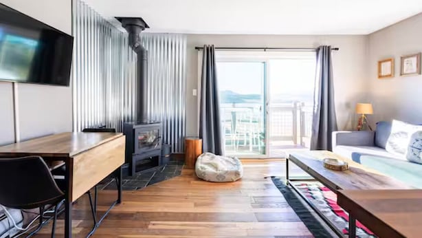 Une chambre d’hôtel moderne avec un bureau en bois, un canapé, un téléviseur fixé au mur et un balcon agrémenté de rideaux.