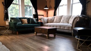 A living room with a green sofa, a beige sofa, a wooden coffee table, and a round table with a gold frame.
