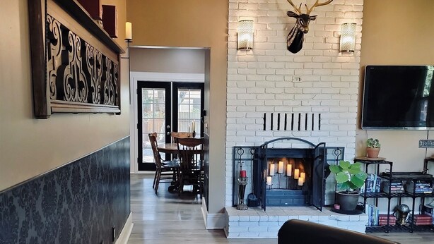 A living room with a fireplace, a mounted deer head, a television, and a dining area with chairs and a table.