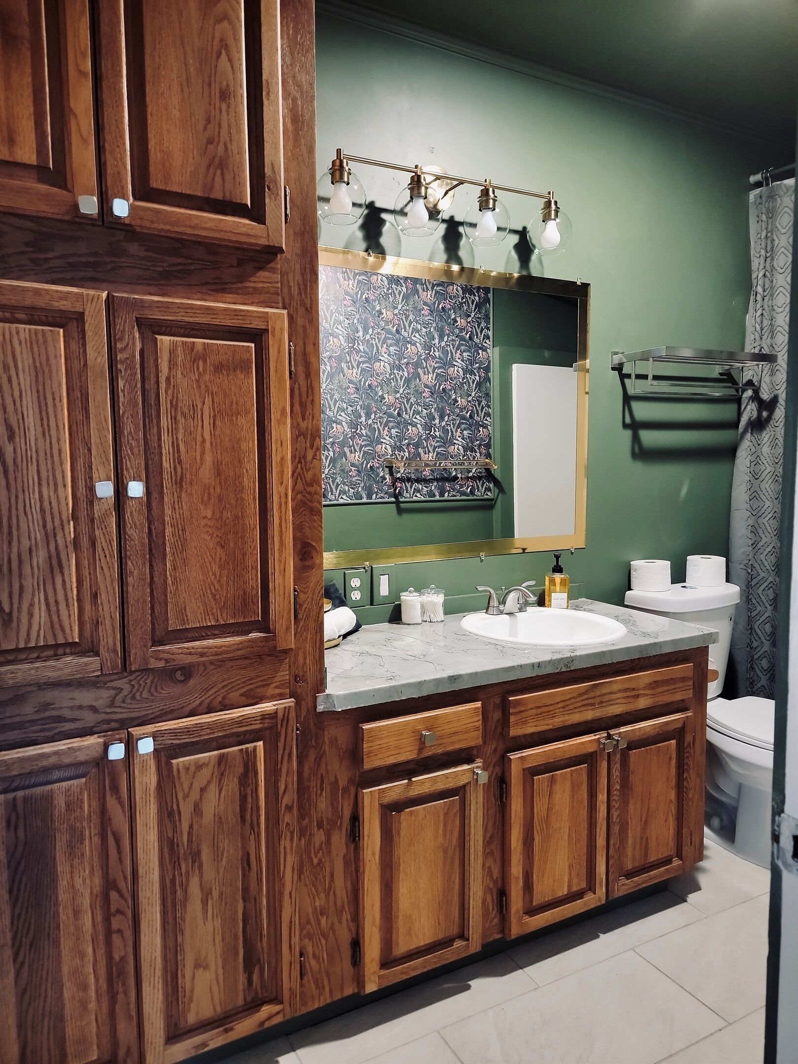 A bathroom with wooden cabinets, a marble sink, a green wall, and a shower curtain.
