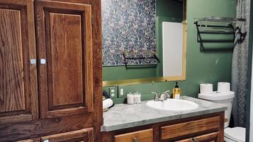A bathroom with wooden cabinets, a marble sink, a green wall, and a shower curtain.