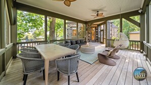 Een overdekt terras buiten, met een houten tafel, rieten stoelen, een ronde salontafel en twee plafondventilatoren.