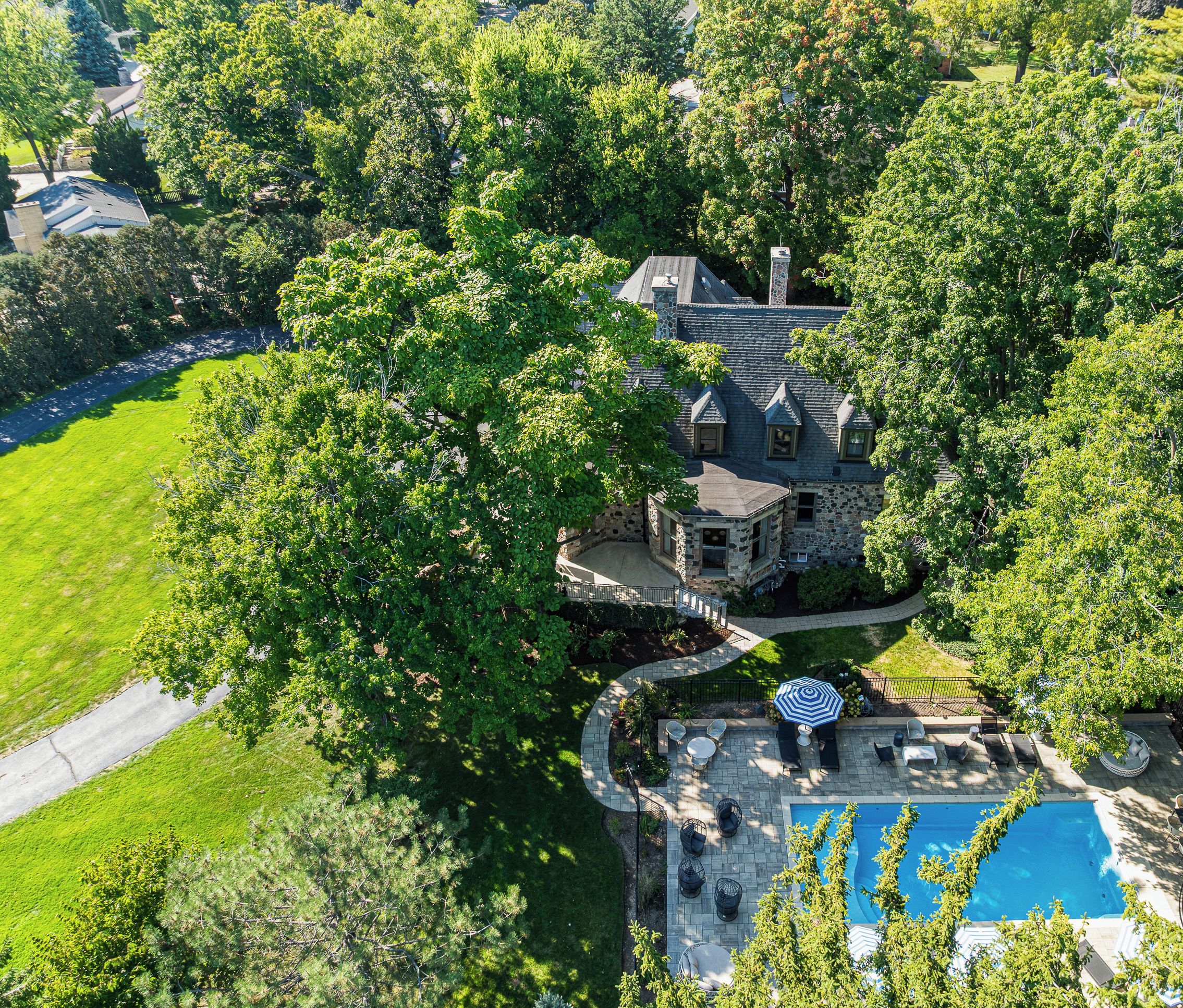 An aerial view of a large estate with a stone house, a swimming pool, and a well-maintained lawn.