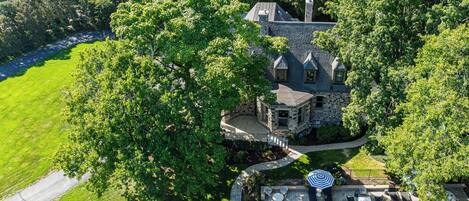 An aerial view of a large estate with a stone house, a swimming pool, and a well-maintained lawn.