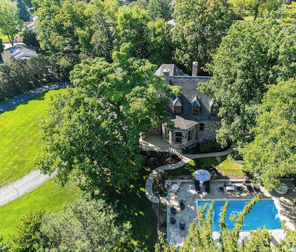 An aerial view of a large estate with a stone house, a swimming pool, and a well-maintained lawn.