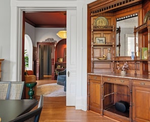 A spacious living room with a wooden cabinet, a dining area with a table and chairs, and a hallway leading to another room.