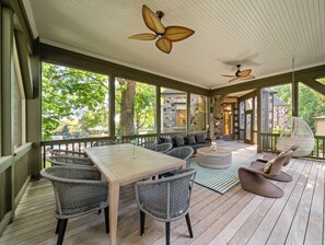 A covered outdoor deck with a wooden table and wicker chairs, a round coffee table, and two ceiling fans.