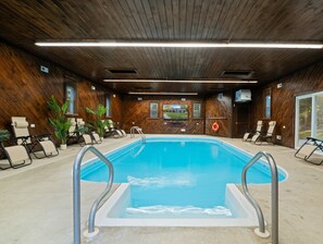 En indendørs swimmingpool med træpaneler, omgivet af liggestole og plantekrukker.