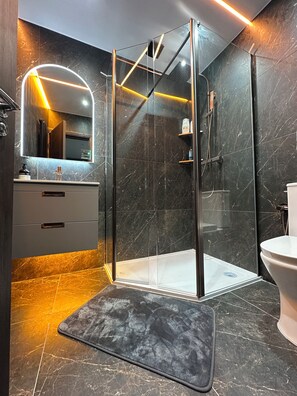 Ein modernes Badezimmer mit einer Duschkabine aus Glas, einem großen Spiegel und einem Marmorboden.
