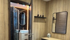 Un baño moderno con pared de paneles de madera, cabina de ducha de vidrio, tocador de madera con espejo y un taburete pequeño.