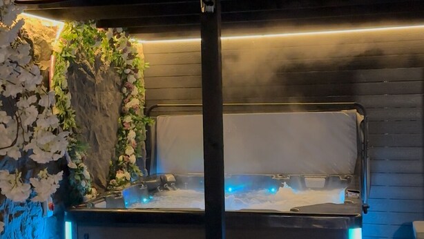 Un área de cocina al aire libre con pared de piedra y una parrilla, iluminada con luces azules y cálidas.
