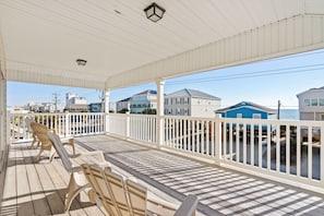 A covered porch with wooden chairs and a railing, overlooking a residential area with houses and a clear sky.