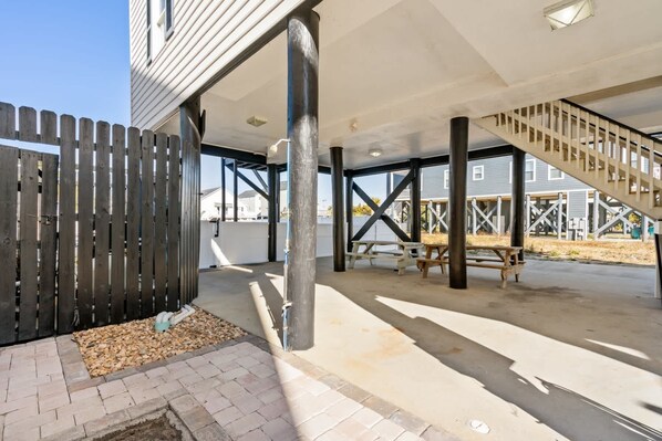 An outdoor covered patio area with a staircase, concrete floor, and a wooden fence. - Tides Like These (Murrells Inlet)