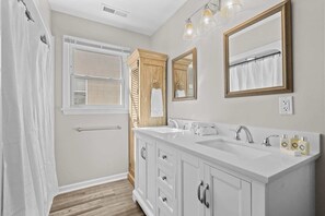 A bathroom with a double sink, wooden cabinets, a towel rack, and a window.