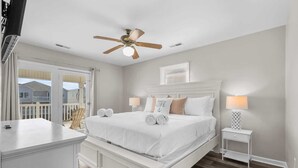 A bedroom with a bed, bedside lamps, a ceiling fan, and a view of the outside. - Tides Like These (Murrells Inlet)