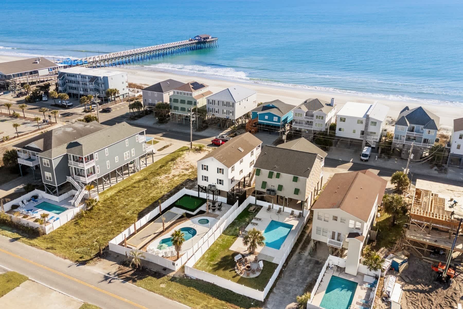 An aerial view of a coastal residential area with houses, a pier, and a beach.