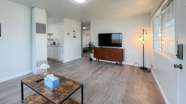 A spacious living room with a wooden floor, a TV, a cabinet, and a table with a remote control. - Cozy 2BR/1BA Suite in a Quiet Renton Area (Renton)