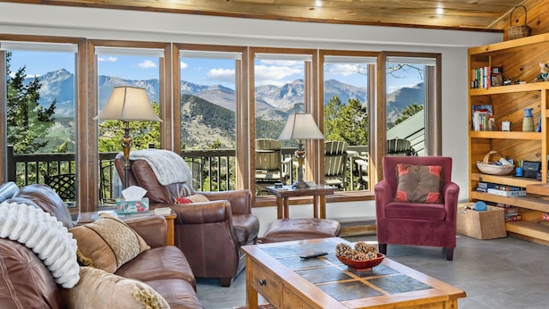Ein gemütliches Wohnzimmer mit Ledermöbeln, einem Holztisch und einer Bücherwand. Große Fenster bieten Blick auf die Berge.